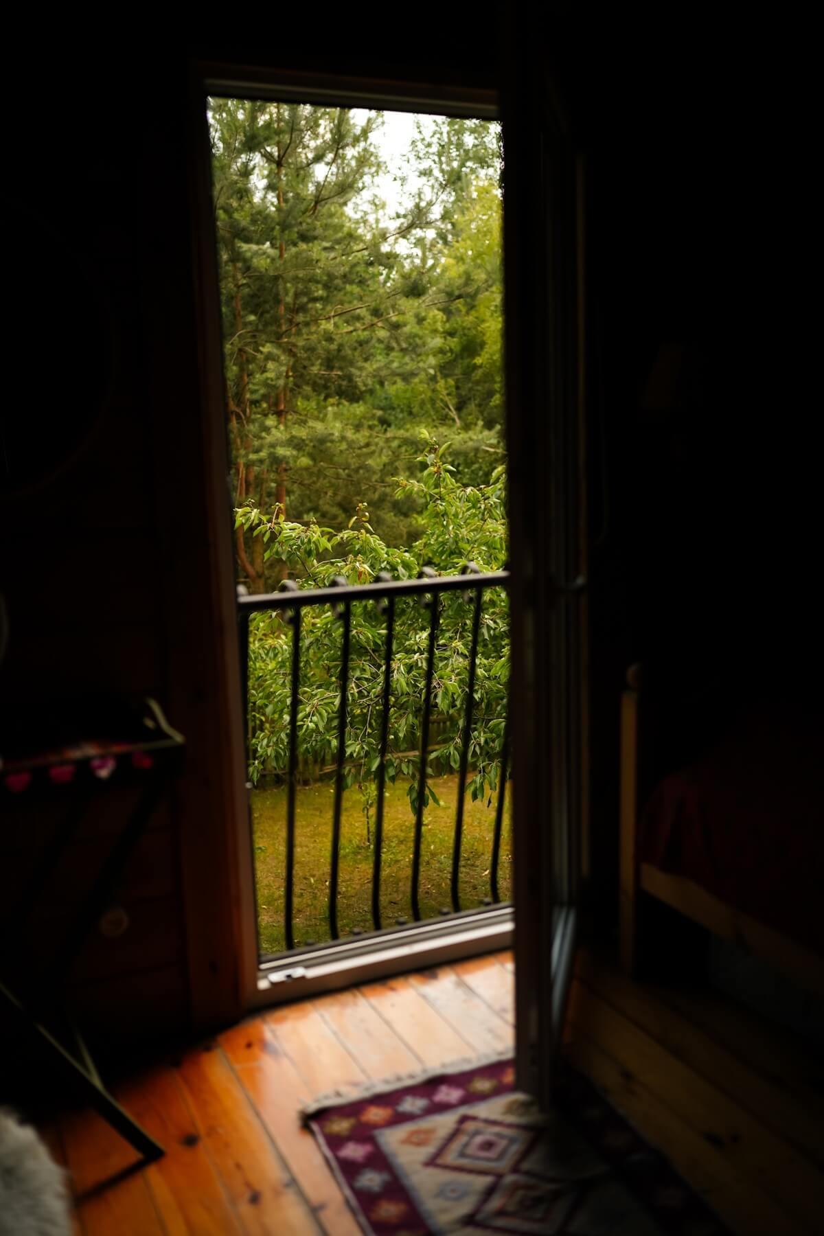 Otwarte drzwi balkonowe na poddaszu z widokiem na zielony ogród