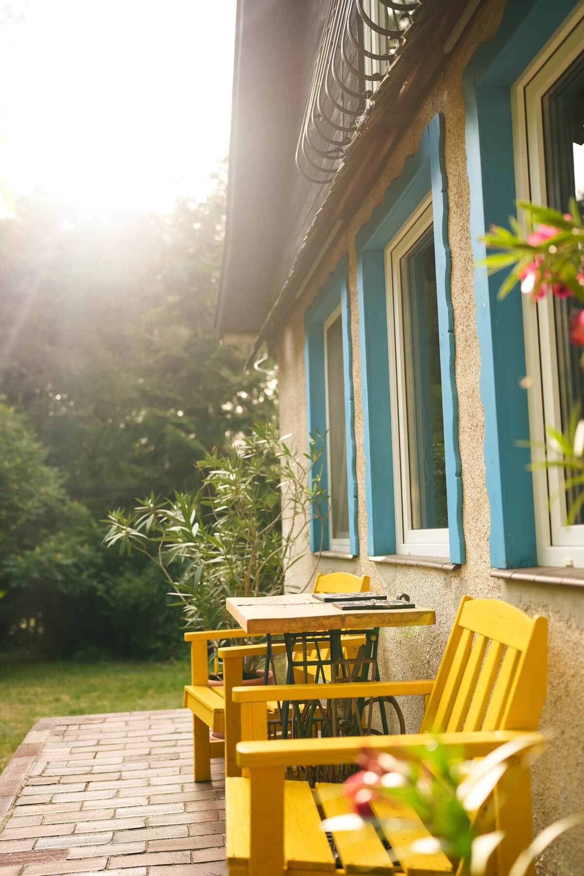 Promienie słoneczne oświetlające taras domku Villa Isabel z żółtymi krzesłami i niebieskimi okiennicami