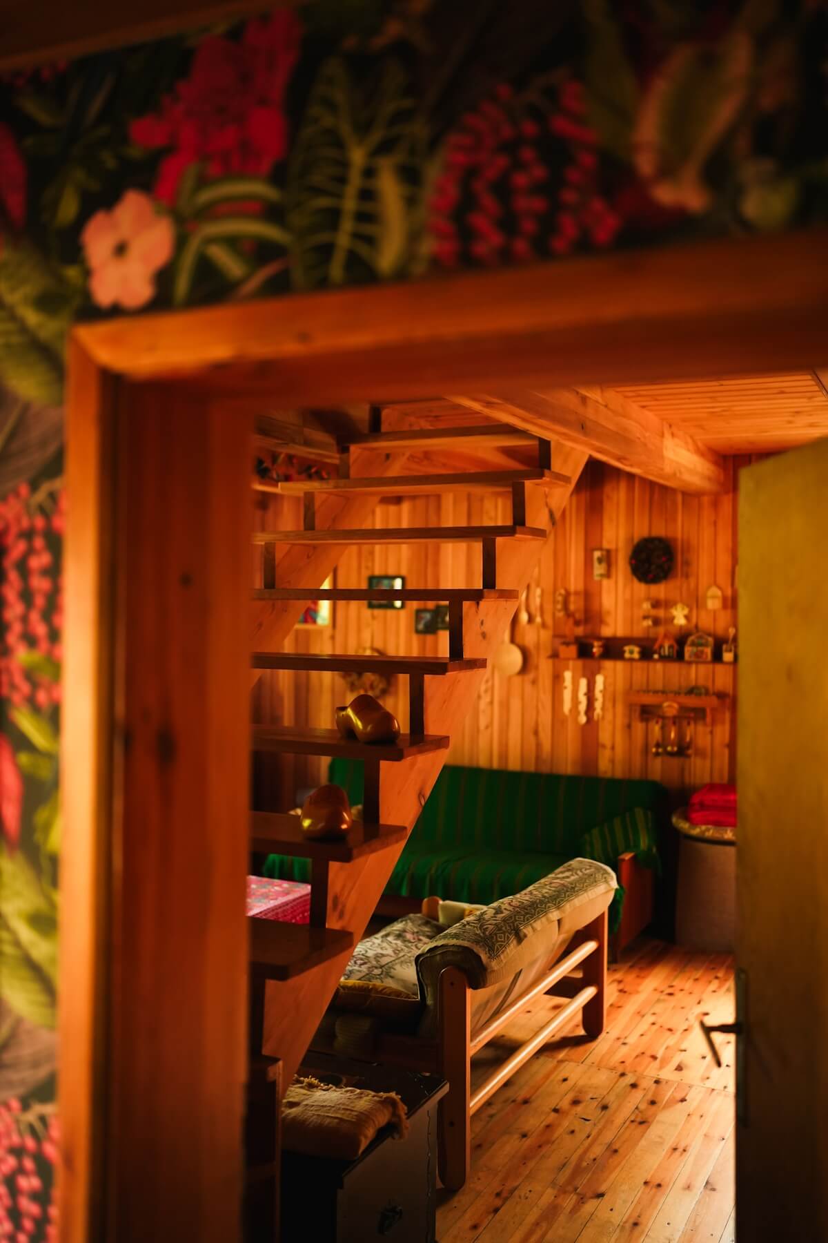 Perspektywa na wnętrze domku z przedsionka. Widok na drewniane schody i dwie kanapy