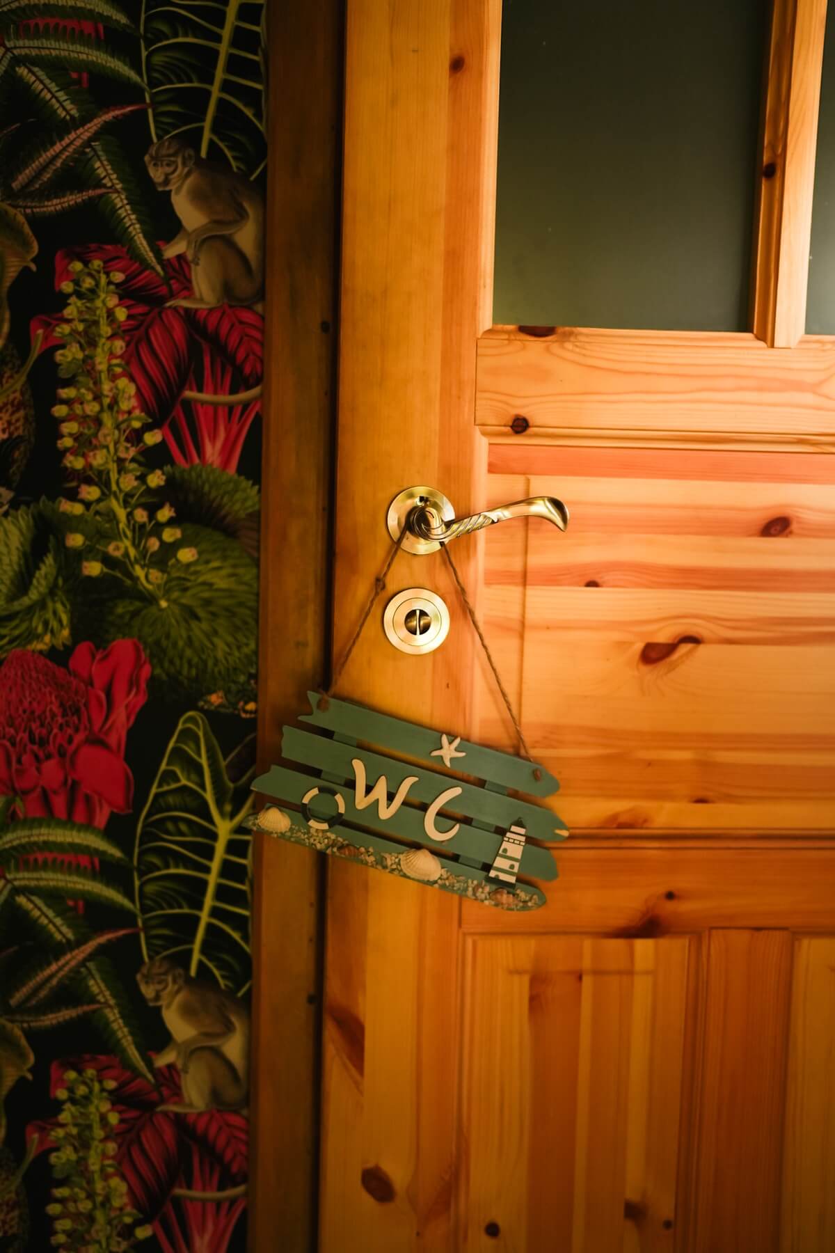 Drewniane drzwi do toalety z wiszącą tabliczką na klamce z napisem WC