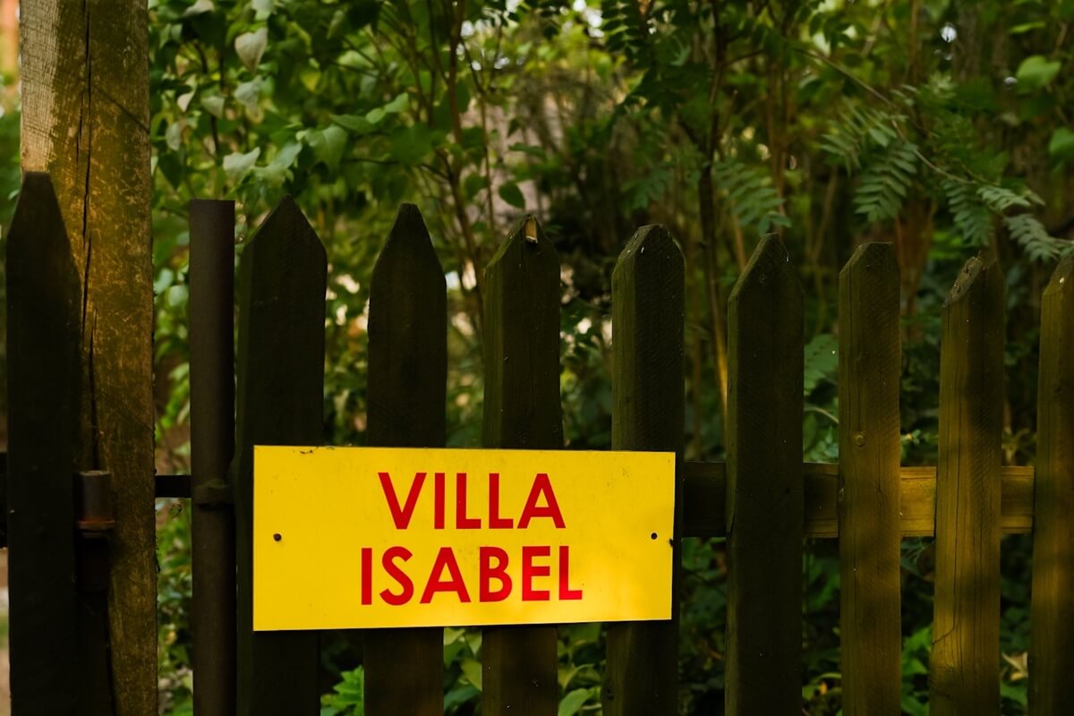 Czerowny napis Villa Isabel na żółtej tablicy przyczepiony do starego, drewnianego płotu